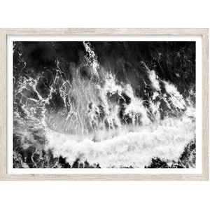 May include: Black and white aerial photograph of a wave crashing in the ocean. The wave is white and the water is dark.