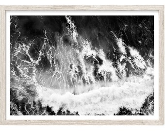 May include: Black and white aerial photograph of a wave crashing in the ocean. The wave is white and the water is dark.