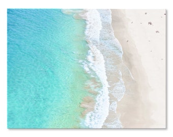 May include: An aerial view of a white sandy beach with turquoise blue water. The waves are crashing on the shore and there are people swimming and sunbathing.