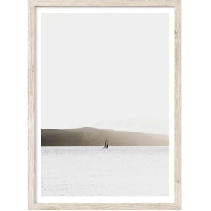 May include: A framed photograph of a sailboat on a calm body of water with a distant mountain range in the background. The sky is a light gray and the water is a light blue.