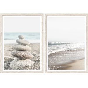 May include: Two framed prints of a beach scene. The left print shows a stack of gray stones on a sandy beach with the ocean in the background. The right print shows a beach with waves crashing on the shore.