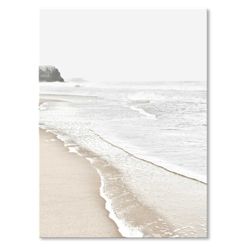 May include: A minimalist photograph of a sandy beach with white foamy waves crashing on the shore. The background features a distant, hazy coastline.