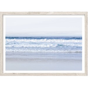 May include: A framed photograph of a seascape with white foamy waves crashing on a sandy beach. The sky is a light blue and the water is a darker blue.