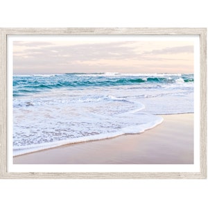 May include: A framed photograph of a beach scene with white foamy waves crashing on the shore. The water is a light blue and the sky is a soft pink and orange.