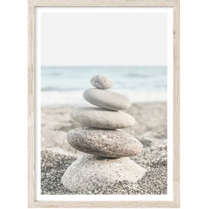 May include: A stack of smooth, gray stones balanced on top of each other on a sandy beach with a blurred ocean in the background.