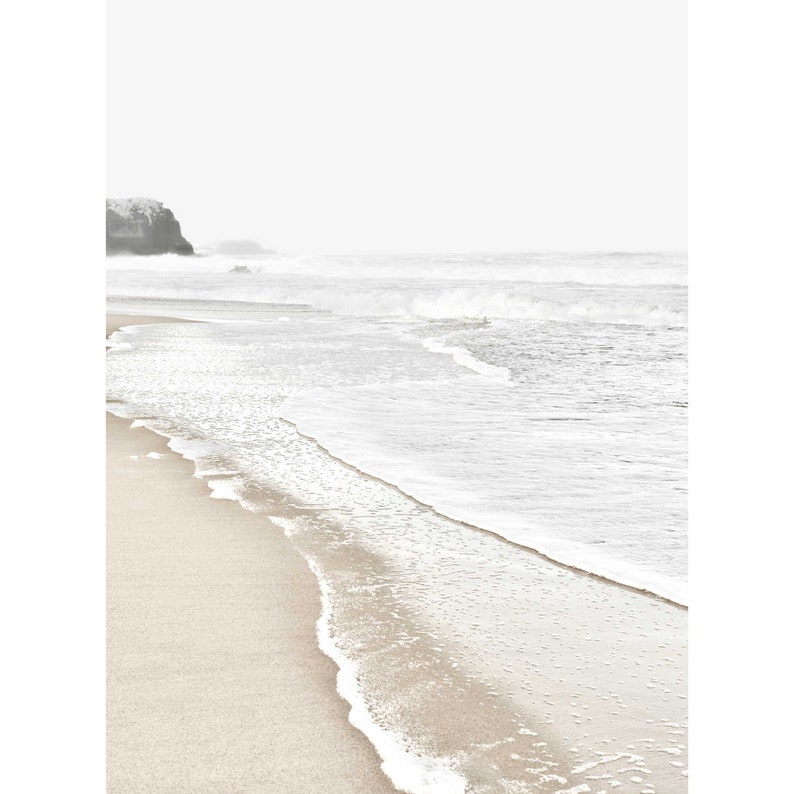 May include: A white sandy beach with foamy waves crashing on the shore. The water is a light blue and the sky is a pale gray.
