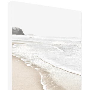 May include: A black and white photograph of a beach scene with waves crashing on the shore. The sand is light brown and the water is white with foam.