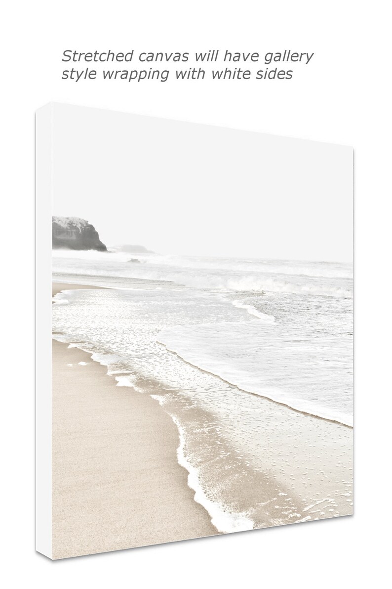 May include: A black and white photograph of a beach scene with waves crashing on the shore. The sand is light brown and the water is white with foam.