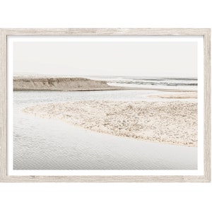 May include: A muted, minimalist photograph of a sandy beach with a river flowing into the ocean. The water is a light blue and the sand is a pale beige. The sky is a soft white.