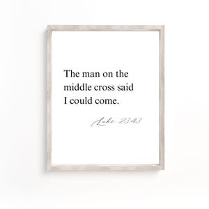 May include: A framed print with a white background and the text "The man on the middle cross said I could come." Below the text is the inscription "Luke 23:43" in a handwritten style font. The frame is a light gray color.