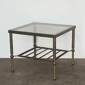 May include: A square side table with a clear glass top and a lower shelf. The metal frame has a bronze finish with brass accents on the legs, which are approximately 51 cm tall.