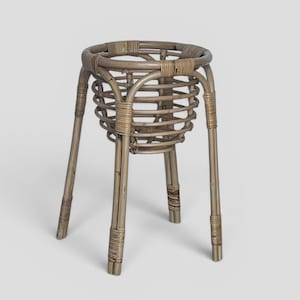 May include: A light brown, woven rattan plant stand with a round top and four long legs. The stand has a cylindrical basket-like structure to hold a plant pot. The legs are reinforced with woven rattan at the base and top.