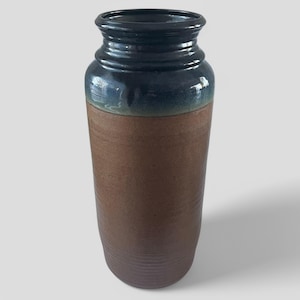May include: A tall, brown ceramic vase with a dark blue glaze on the top half. The vase has a slightly flared opening and a rounded bottom.