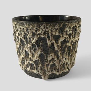 May include: A black ceramic planter with a white textured design. The planter has a rough, uneven surface and a rounded shape.