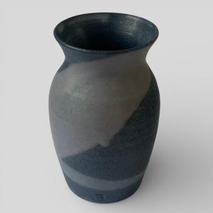 May include: A handmade ceramic vase in dark blue and grey. The vase has a wide opening and a rounded body with a textured surface. The design features a diagonal stripe pattern in varying shades of blue and grey. The vase is approximately 20 cm tall.