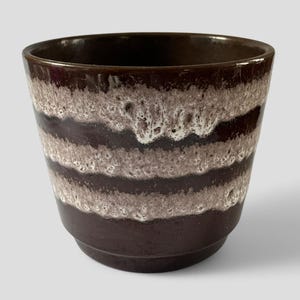 May include: A brown ceramic plant pot with a textured, layered design. It has horizontal bands of dark brown, light brown, and white, creating a unique pattern. The top and base are a solid, darker brown colour.