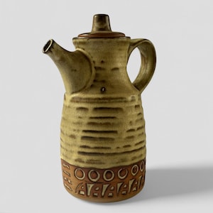May include: A brown and yellow ceramic teapot with a lid and a handle. The teapot has a textured surface and a decorative band around the bottom.
