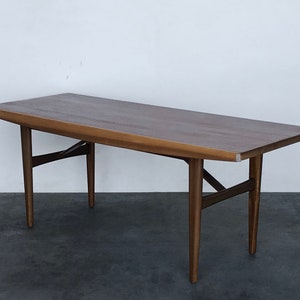 May include: A mid-century modern coffee table with a rectangular wooden top and a unique angled design. The table has four legs with a cross-shaped support structure.
