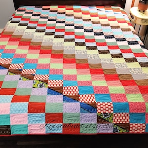May include: A patchwork quilt with a variety of colors and patterns, including red, pink, blue, green, and brown. The quilt is quilted with a pattern of curved lines. The quilt is on a bed with a wooden headboard. The text "Kyescabinet.etsy.com" is visible in the lower right corner of the image.