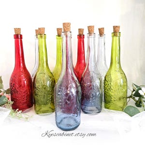 May include: A collection of decorative glass bottles in various colors, including red, green, and blue, each topped with a cork stopper. The bottles have a textured surface and are arranged on a white surface. The Etsy shop name "Kyescabinet.etsy.com" is visible.