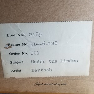 Op de afbeelding: Een wit label met zwarte tekst met de details van een ingelijst kunstwerk. Het label vermeldt: "Line No. 2189", "Frame No. 314-6-L28", "Order No. 101", "Subject Under the Linden", "Artist Bartsch".