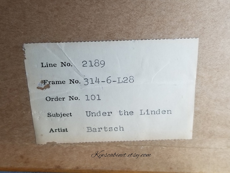 Op de afbeelding: Een wit label met zwarte tekst met de details van een ingelijst kunstwerk. Het label vermeldt: "Line No. 2189", "Frame No. 314-6-L28", "Order No. 101", "Subject Under the Linden", "Artist Bartsch".