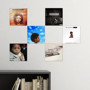 May include: A collage of five album covers featuring hip hop artists. The covers are arranged in a grid pattern on a white wall. The album covers feature Lil Wayne, Lauryn Hill, Eminem, The Notorious B.I.G., and The Beastie Boys.