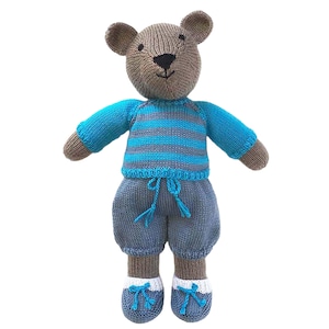 May include: A handmade knitted teddy bear wearing a blue and gray striped sweater, blue shorts with a drawstring, and blue shoes with white trim and blue bows. The bear has a brown head, arms, and feet.