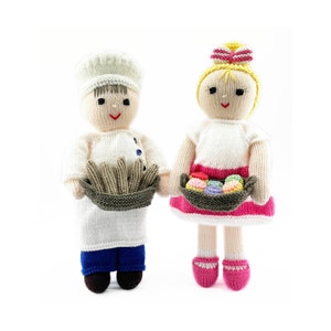 May include: Two knitted dolls, one wearing a white chef's hat and holding a basket of bread, the other wearing a pink dress and holding a basket of colorful pastries.