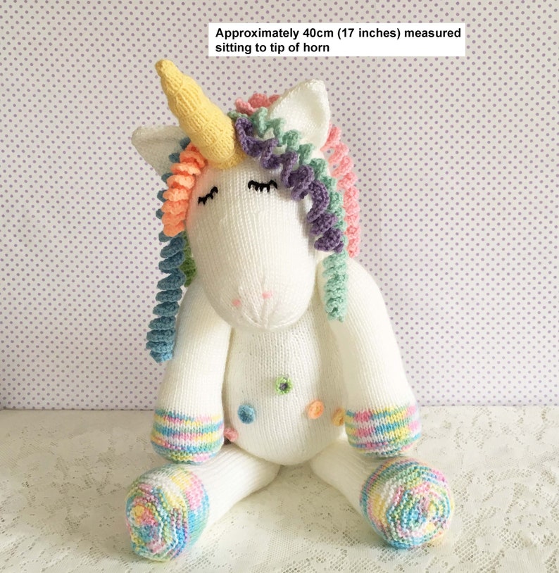 May include: A white knitted unicorn doll with a yellow horn, rainbow mane, and multi-colored accents. The doll is approximately 17 inches tall. It has closed eyes and colorful details on the feet and body.
