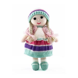 May include: A knitted doll with a pink and purple striped dress, a white sweater, and a blue and green hat. The doll has blonde hair and a pink bow.