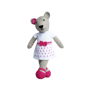 May include: A knitted mouse doll wearing a white dress with pink polka dots and a pink bow. The doll has gray fur, pink accents on the ears, and is wearing pink shoes. The doll is standing against a white background.
