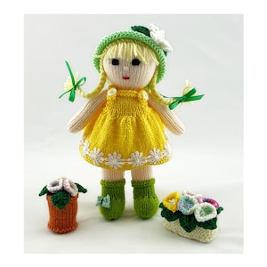 May include: A knitted doll wearing a yellow dress with white trim, a green and white hat with a white flower, and green boots. The doll is holding a bouquet of flowers in one hand and a potted plant in the other.