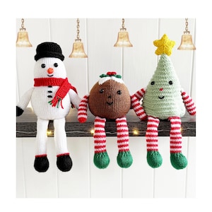 Puede incluir: Tres figuras de ganchillo navideñas: un muñeco de nieve blanco con sombrero negro y bufanda roja, un pudin redondo marrón con glaseado blanco y bayas rojas, y un árbol de Navidad verde claro con una estrella amarilla, todos con extremidades a rayas.