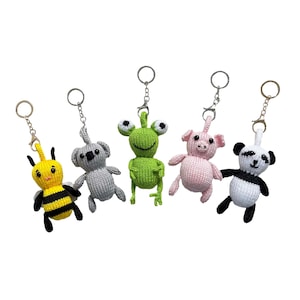 May include: Five knitted animal keyrings: a yellow and black bee, a grey koala, a green frog, a pink pig, and a black and white panda. Each keyring has a silver-coloured metal ring and clasp for attaching to keys or bags.
