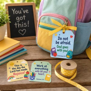 Op de afbeelding: Drie rechthoekige papieren labels met afgeronde hoeken, kleurrijke illustraties en religieuze teksten. Eén label is met een geel lint aan een pastelkleurige rugzak bevestigd. De labels tonen teksten zoals Do not be afraid, God goes with you, This is the day the Lord has made en Work at everything with all your heart.