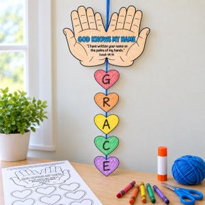 May include: A hanging craft project featuring two paper hands with the text GOD KNOWS MY NAME and Isaiah 49:16, connected to a vertical string of five coloured paper hearts spelling GRACE in black letters, with a colouring sheet and supplies.