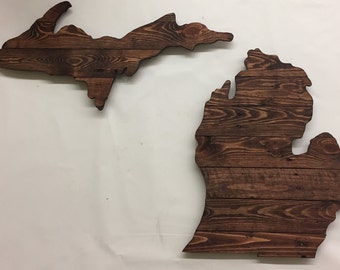 May include: Two wooden wall decor pieces shaped like the state of Michigan. The upper piece is the Upper Peninsula and the lower piece is the Lower Peninsula. Both pieces are made of dark brown wood.