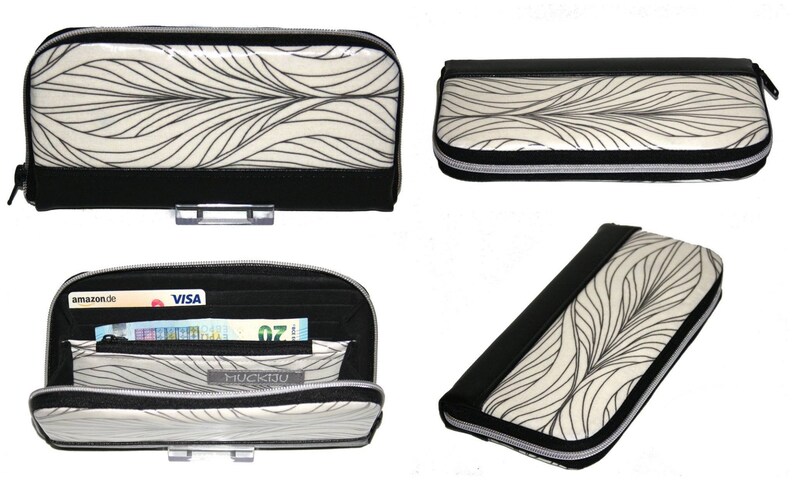Op de afbeelding: Een zwarte en cr&egrave;mekleurige portemonnee met een vloeiend, bladvormig patroon. De portemonnee heeft een zwarte rits en afwerking en wordt in meerdere weergaven getoond, waaronder een open weergave met kaarten en contant geld.