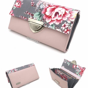 Op de afbeelding: Een roze portemonnee met een bloemenpatroon op de flap. De portemonnee heeft een zilveren sluiting en een grijs bloemenpatroon. De binnenkant is grijs en roze, met meerdere compartimenten voor kaarten en contant geld.