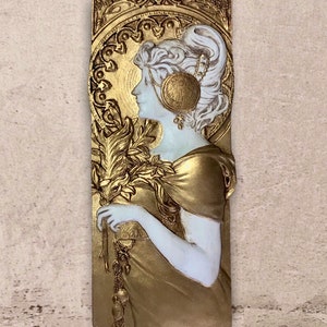 Peut inclure: Une sculpture en relief dorée et blanche d'une femme avec un motif floral et une bordure décorative.