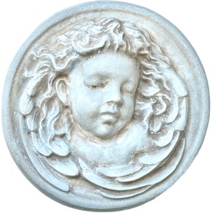 May include: A white ceramic plaque featuring a bas-relief sculpture of a cherub's face with closed eyes and wings.
