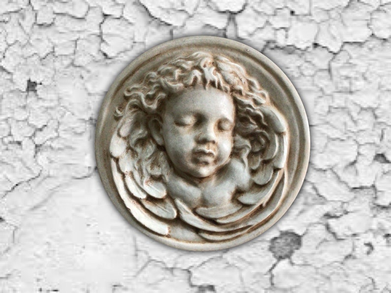 May include: A white ceramic plaque with a bas-relief sculpture of a sleeping angel with wings.