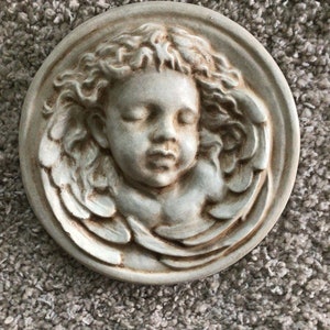 May include: A white ceramic wall plaque with a bas-relief sculpture of a sleeping angel with wings.