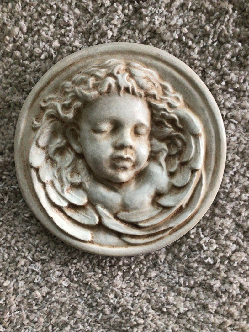 May include: A white ceramic wall plaque with a bas-relief sculpture of a sleeping angel with wings.