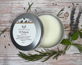以下が含まれることがあります： Heavenly Bliss Skincareの「All Natural Vapor Rub」の、蓋が開いた丸い銀色の缶。 ココナッツオイルやシアバターなどの成分がラベルに記載されています。 製品は59mlです。 ローズマリーとラベンダーの小枝が缶の周りに配置されています。