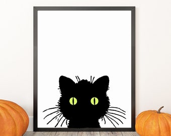 May include: A framed black and white print of a black cat silhouette with yellow eyes. The print is set against a white wall, with three orange pumpkins in front, creating a Halloween theme.