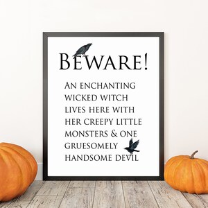 Puede incluir: Un cartel enmarcado con temática de Halloween con el texto "BEWARE!" y un poema sobre una bruja malvada, monstruos y un diablo. Se representan dos pájaros negros. Tres calabazas naranjas están en primer plano.