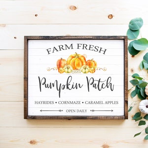 May include: A wooden framed sign with the words "Farm Fresh Pumpkin Patch" in black script. The sign features watercolor pumpkins in shades of orange and yellow. Additional text includes "Hayrides, Cornmaze, Caramel Apples, Open Daily."