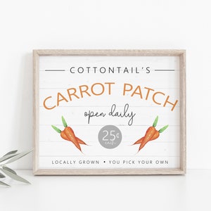 May include: A sign for a carrot patch called "Cottontail's Carrot Patch" with a white background and brown wood frame. The sign says "open daily" and "25¢ each". It also says "Locally Grown - You Pick Your Own".
